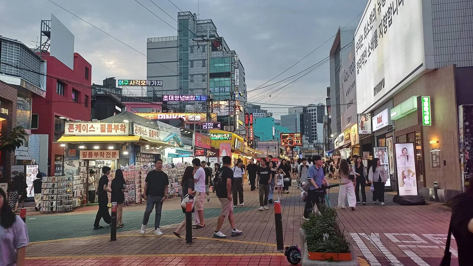 People walking along a pedestrian street lined with small shops in Hongdae, Seoul, at dusk