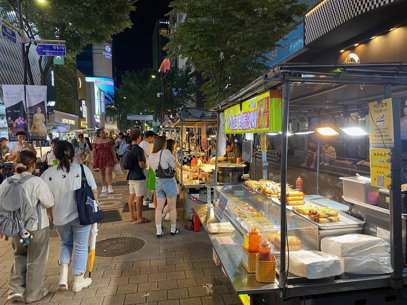夏の夕方、ソウルの明洞の夜市に並ぶ屋台と歩行者