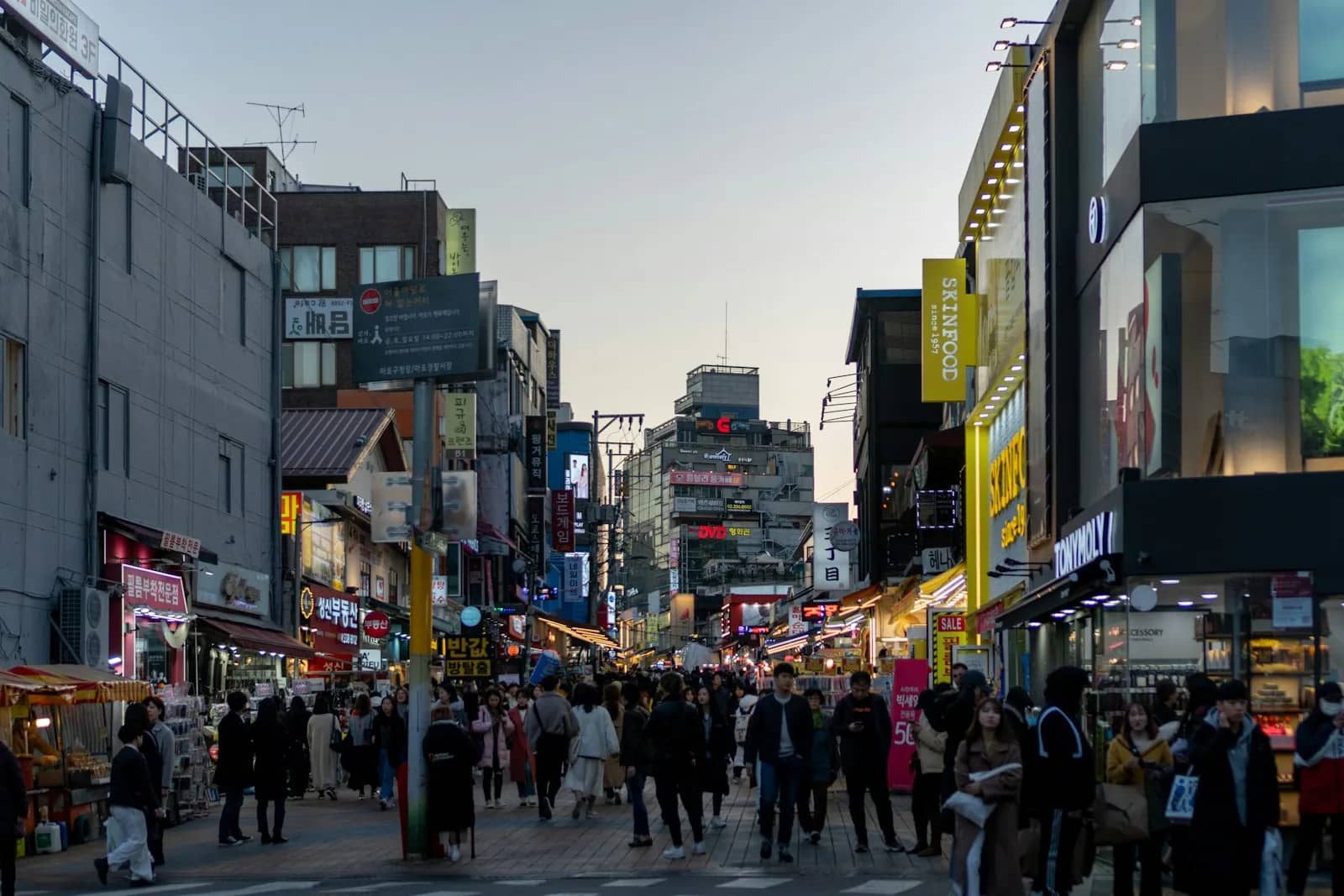 Hongdae Street in Seoul lined with shops and a crowd of walkers in early evening