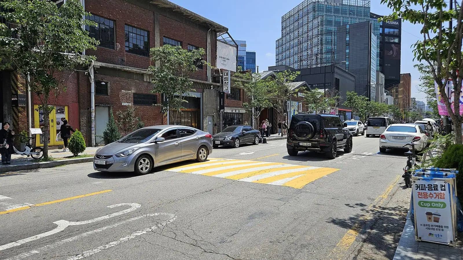 Street in Seongsu-dong, Seoul, with old red brick warehouse buildings, street trees and newer glass towers behind