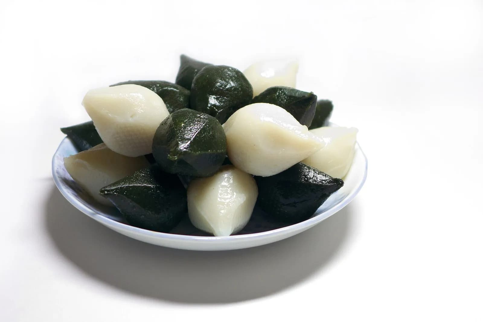 White and dark green songpyeon rice cakes piled on a small white plate