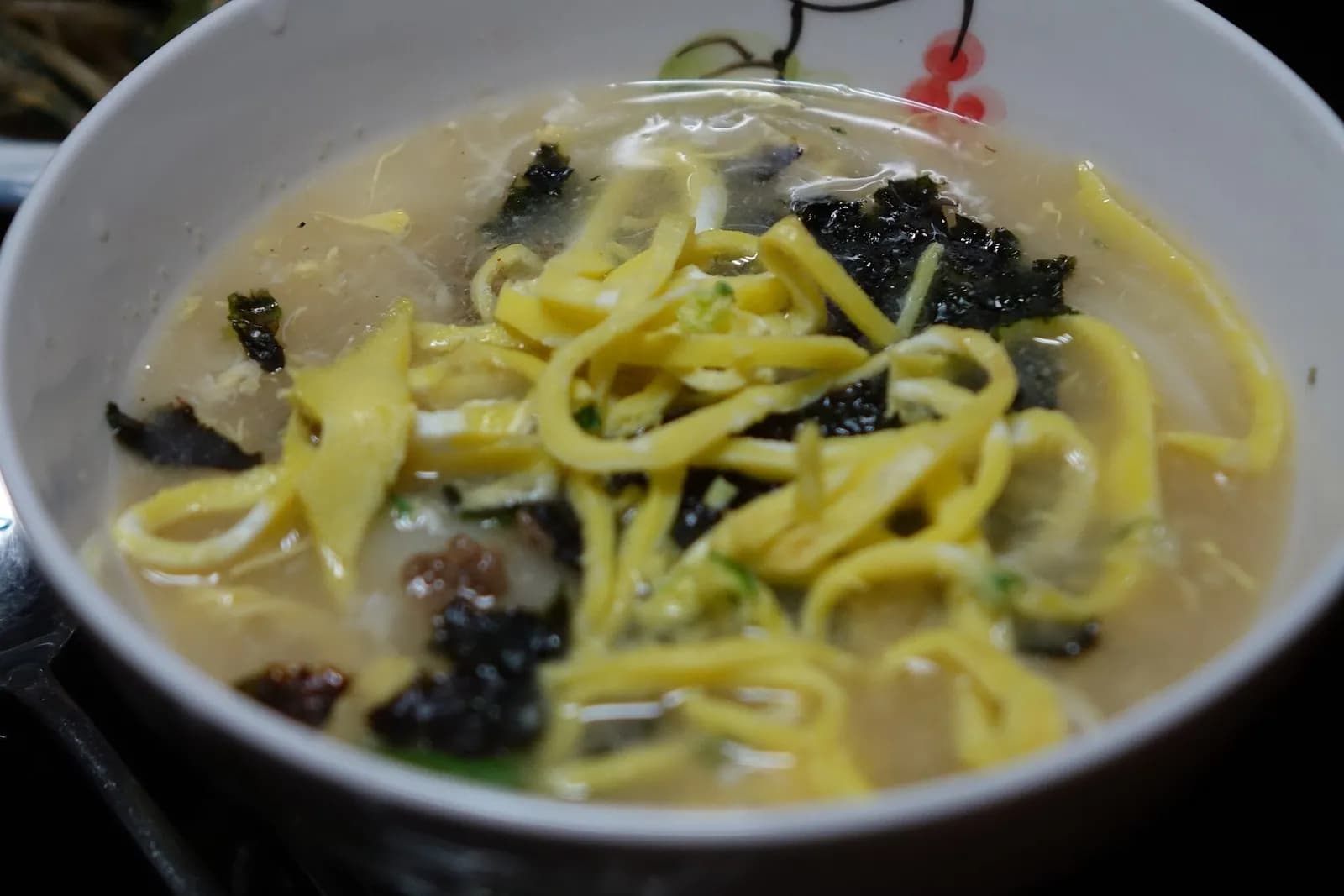 Close view of tteokguk with sliced rice cakes, egg strips and dried seaweed