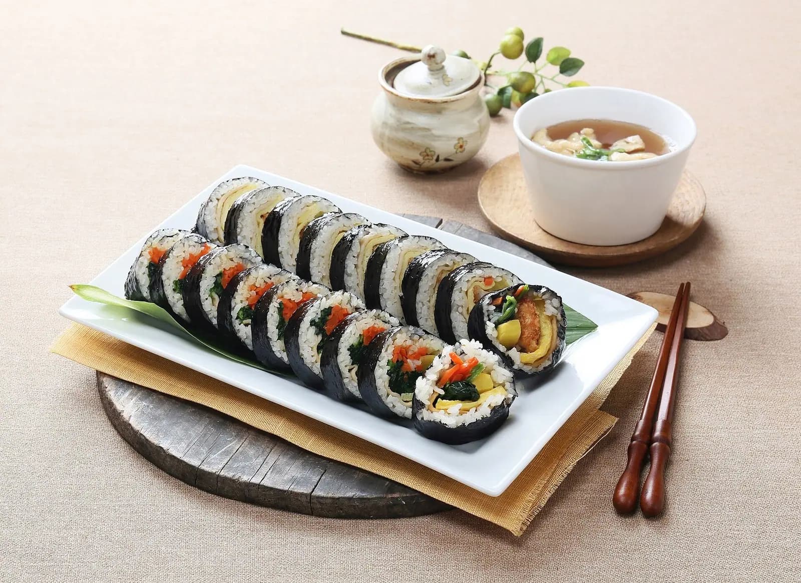 Sliced gimbap seaweed rice rolls on a white plate with a small bowl of soup
