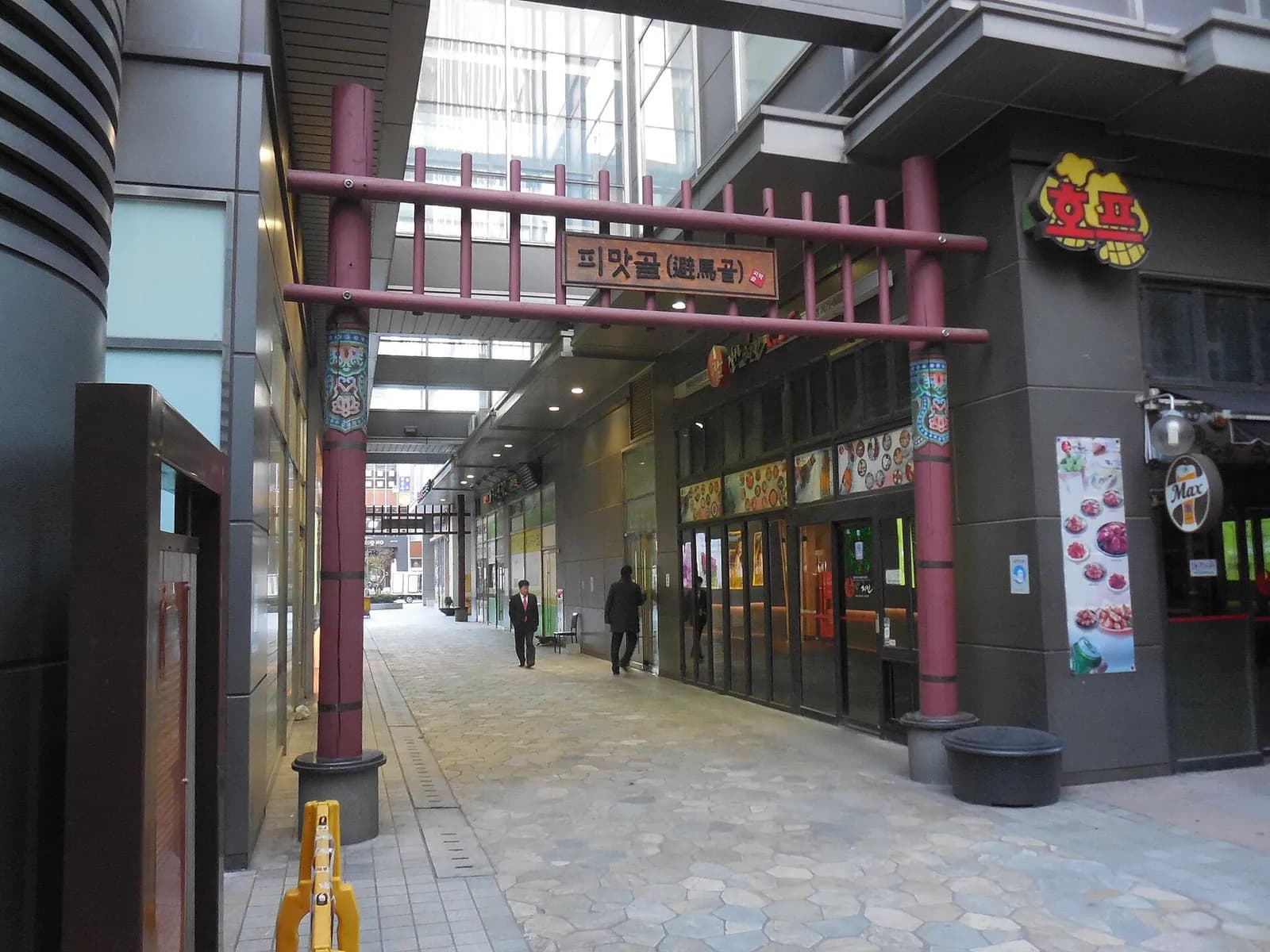 Red wooden gate marking the Pimatgol lane between restaurant fronts in Jongno, Seoul