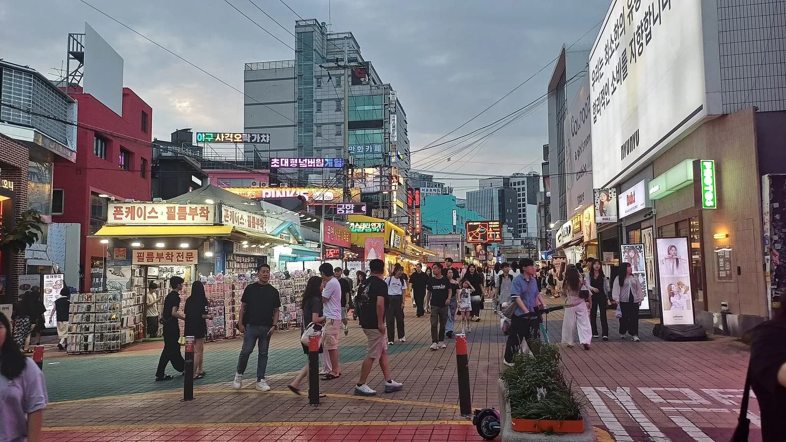 People walking along a pedestrian street lined with small shops in Hongdae, Seoul, at dusk