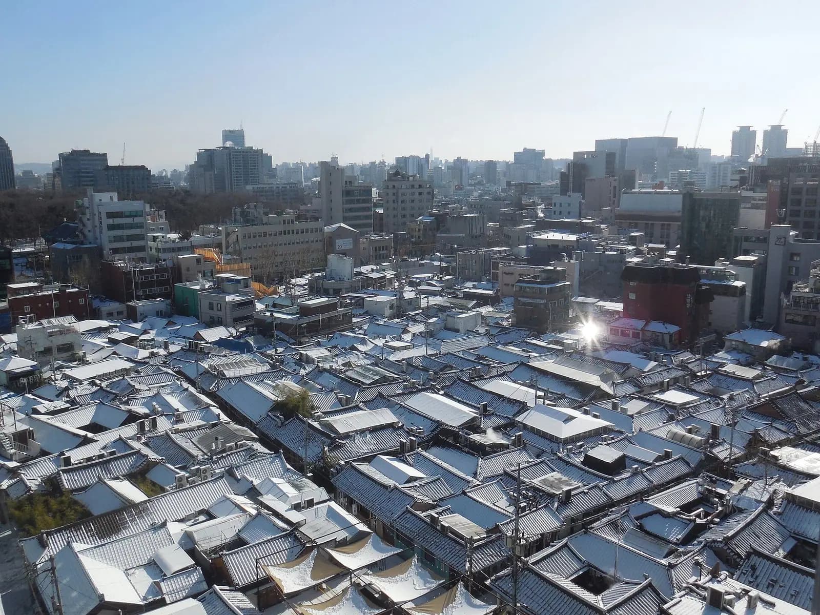 Dense grid of tiled hanok rooftops in Ikseon-dong seen from above, Seoul towers behind