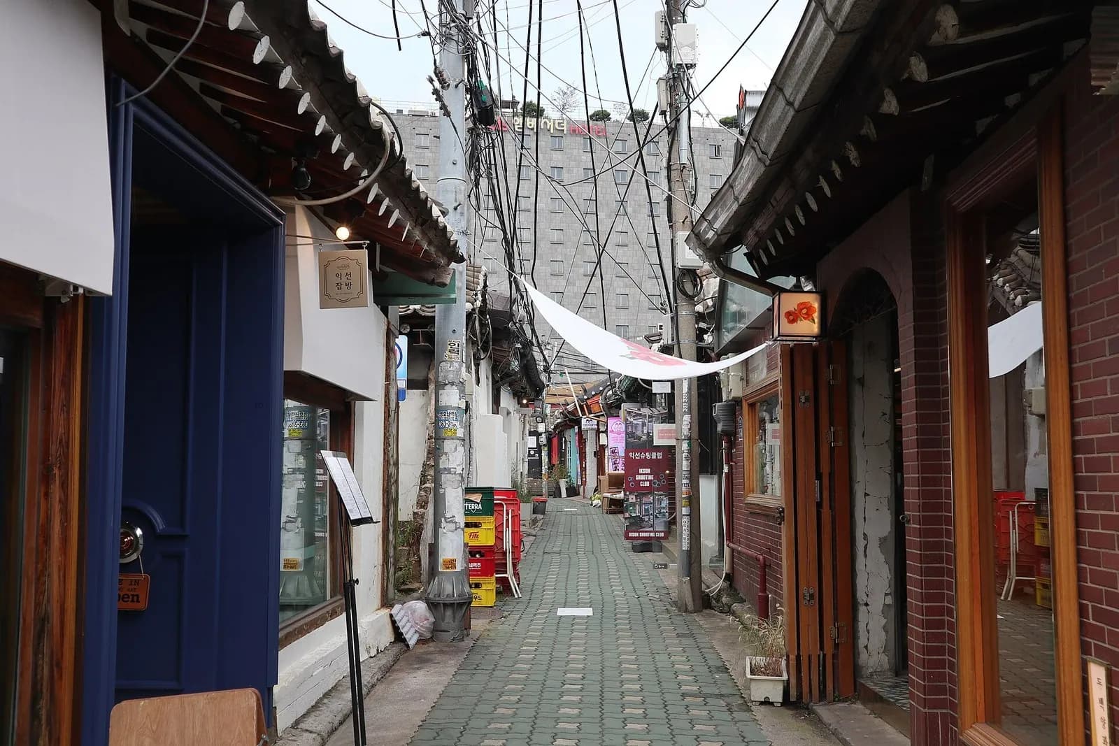 Very narrow paved lane in Ikseon-dong between hanok shopfronts, overhead cables and signs