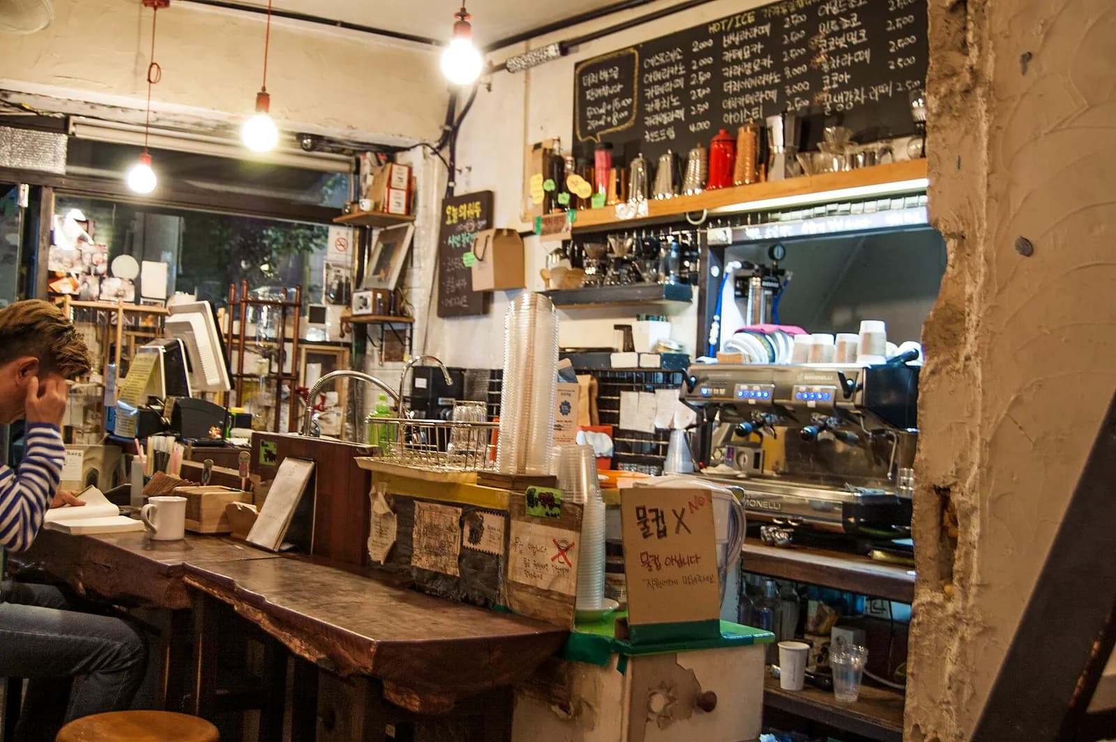 Counter of a bookshop cafe in Seoul with an espresso machine, stacked cups and a chalkboard menu