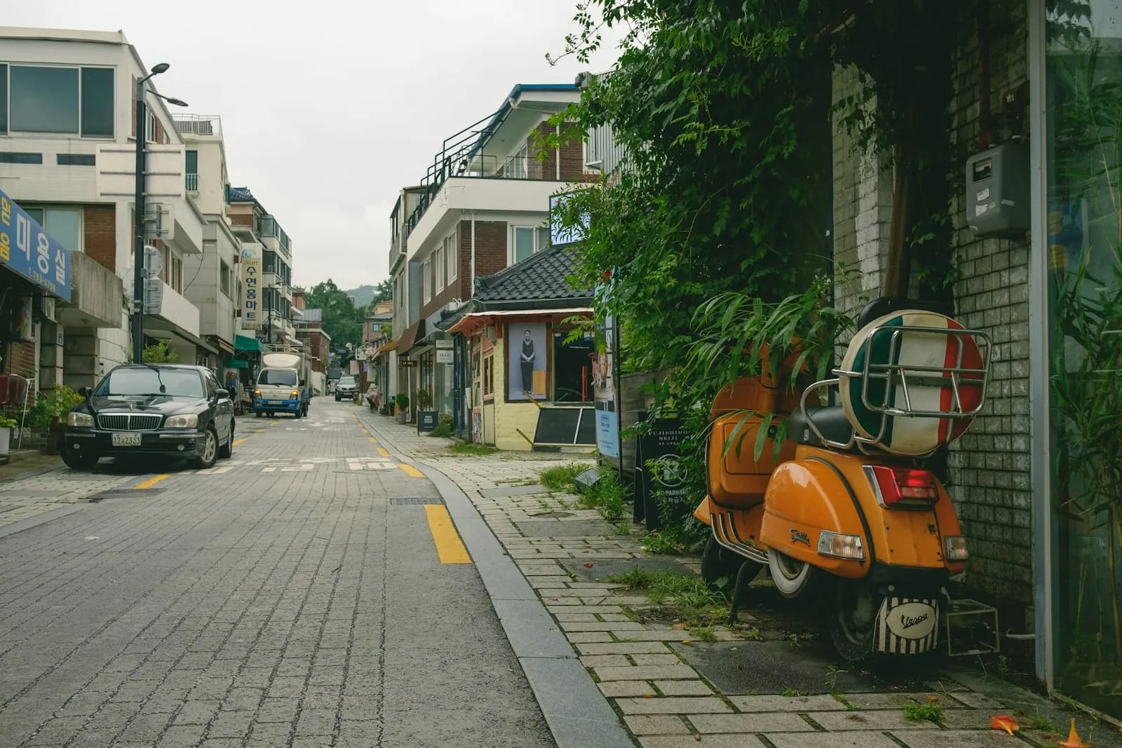 Quiet Seoul residential street with low houses and an orange scooter parked by a wall