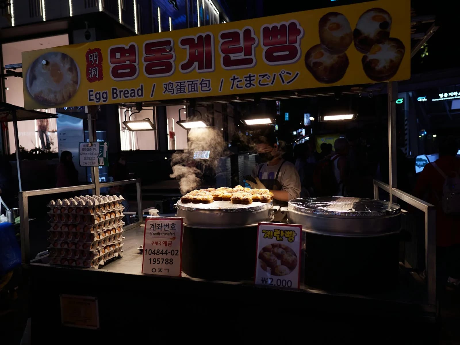 Street stall selling egg bread from round griddles on a Seoul street at night