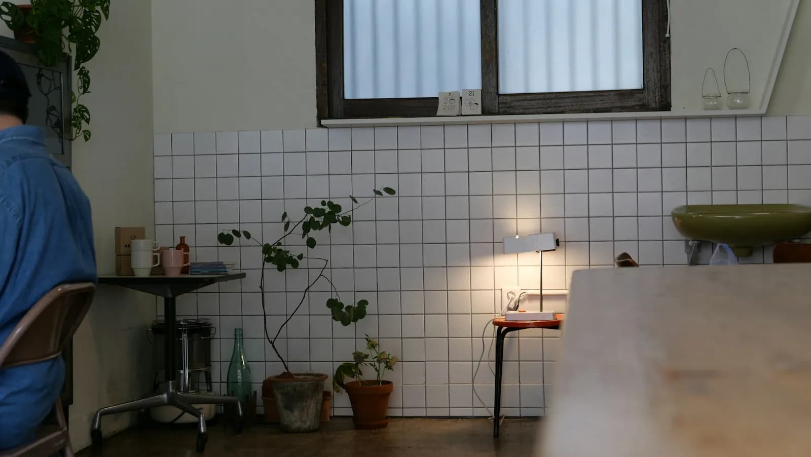 Quiet cafe corner with white tiled walls, a small lamp and window light