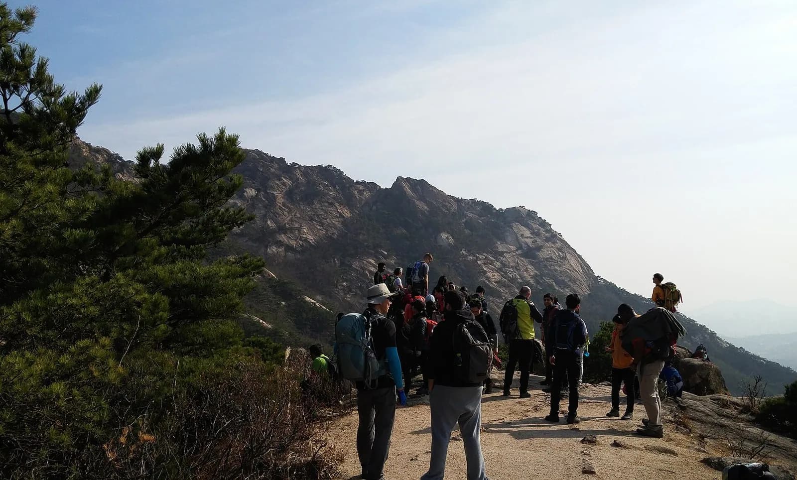 Group of hikers with backpacks stand on a Bukhansan ridge below granite peaks