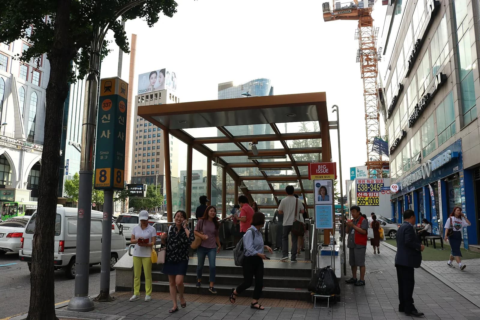 Glass-roofed entrance of Sinsa Station exit 8 with pedestrians on the sidewalk
