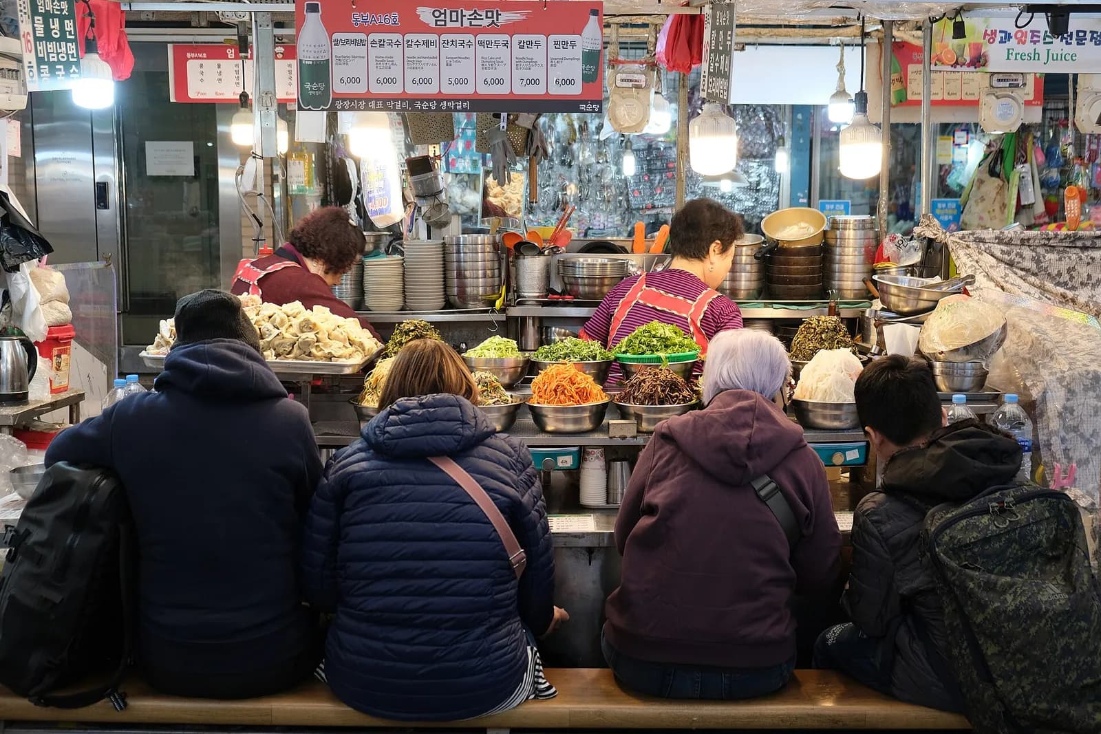 店の人が料理を出す中、ソウルの広蔵市場の屋台でベンチに座る客の後ろ姿