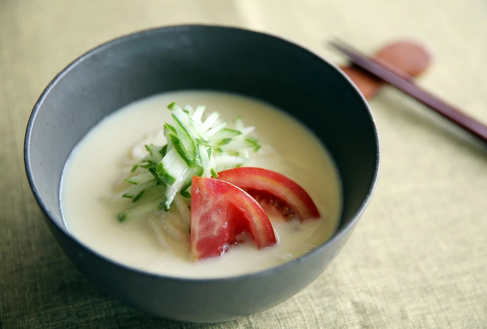 Bowl of kongguksu cold soy milk noodles topped with cucumber and tomato