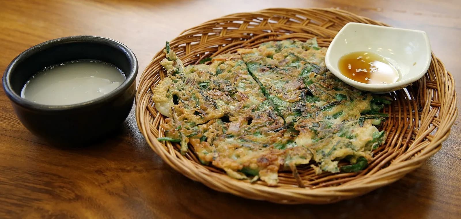Green onion pancake in a wicker basket beside a bowl of makgeolli rice wine