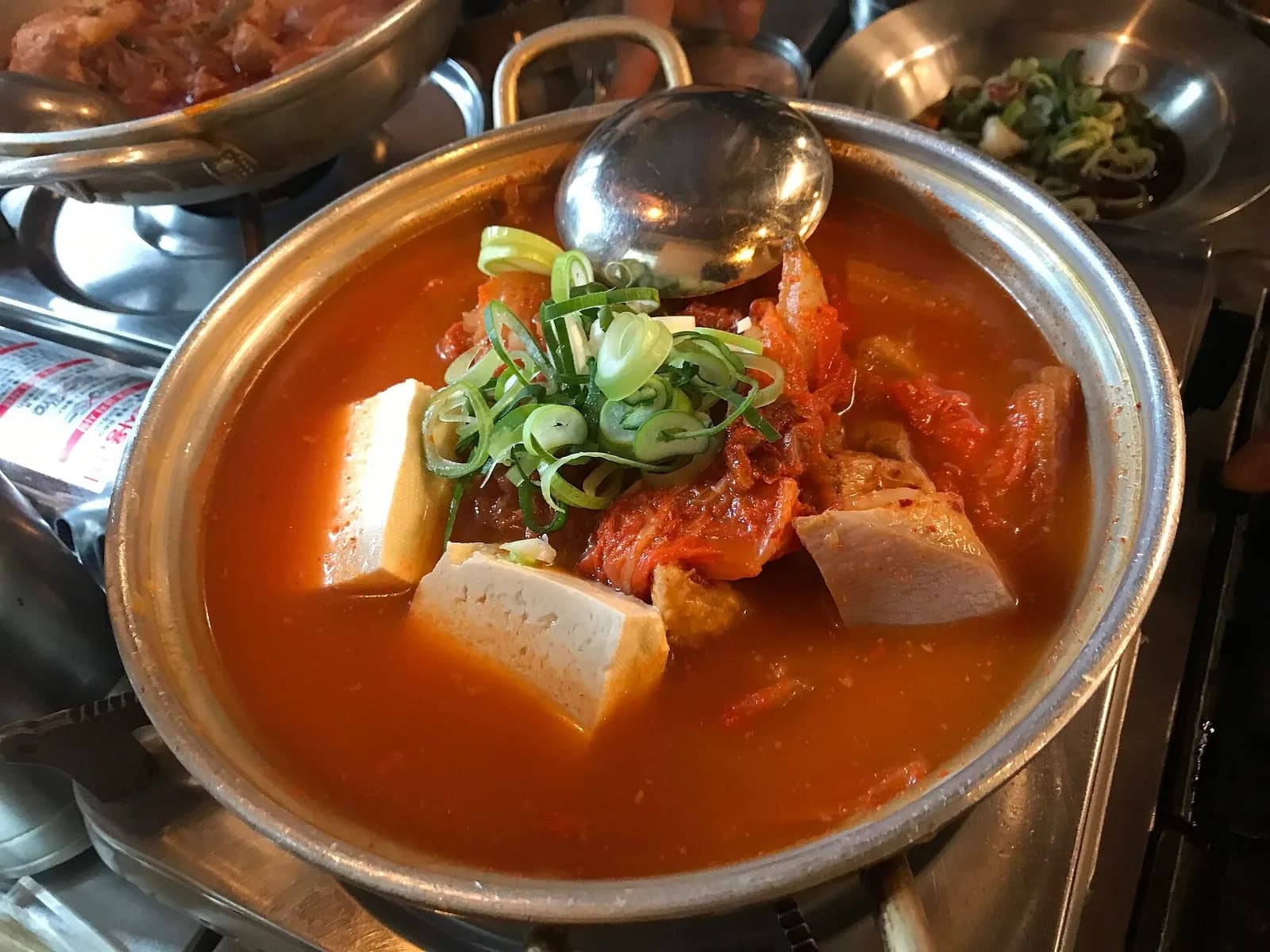 卓上コンロにのった金属鍋の、豆腐とねぎ入りのキムチチゲ
