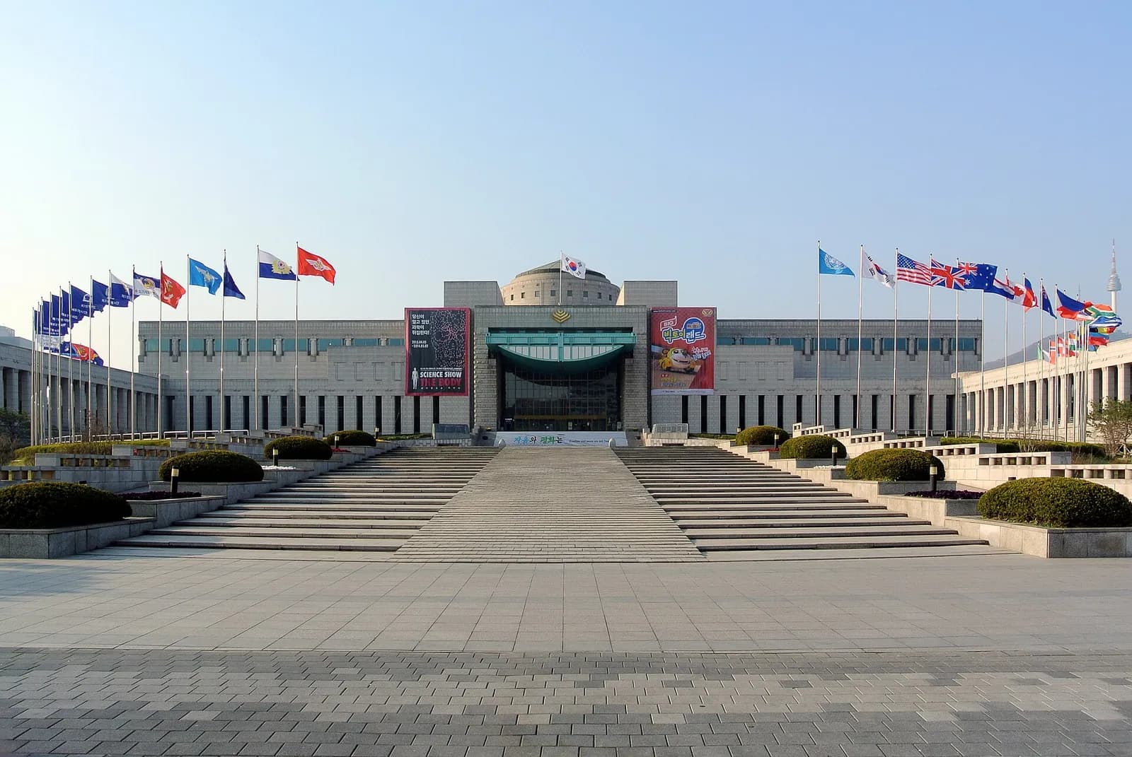 国旗が並ぶ広い階段状の広場の奥に建つ戦争記念館の本館