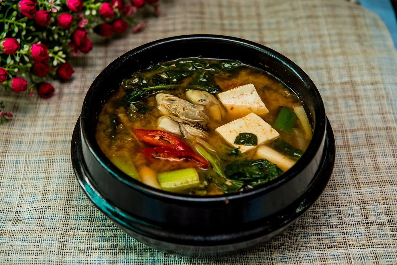 Doenjang jjigae soybean paste stew with tofu, greens and chili in a black stone pot
