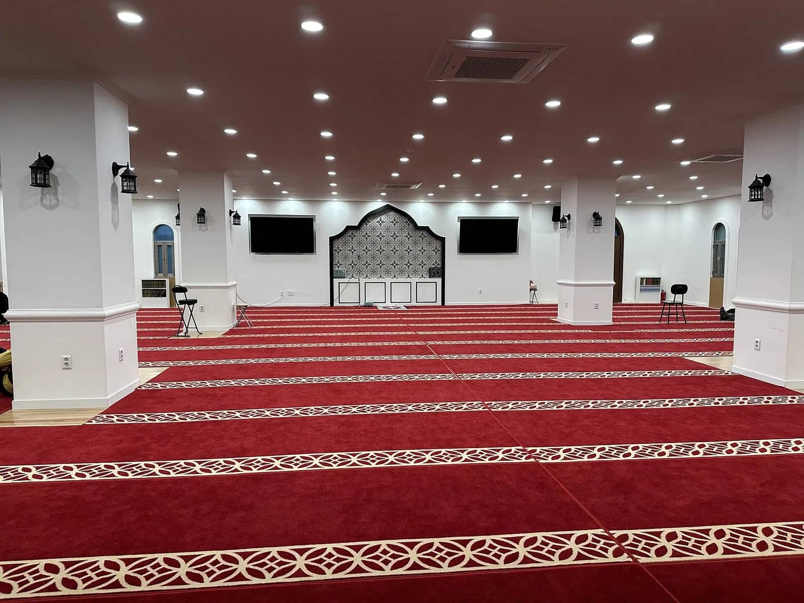 Prayer hall of Seoul Central Mosque with red patterned carpet, white columns and mihrab