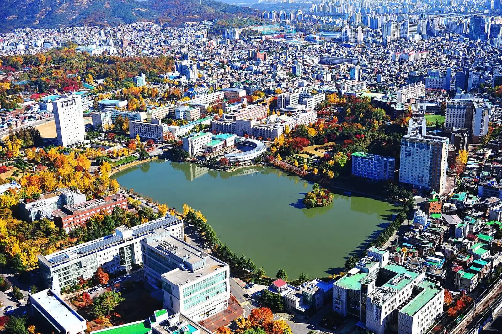 Aerial view of Konkuk University campus and Ilgam Lake in autumn, surrounded by dense city blocks