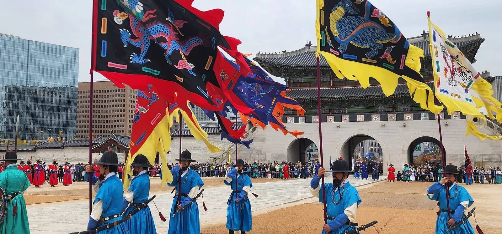 Royal guards in blue robes carry dragon flags in front of Gwanghwamun gate, Seoul