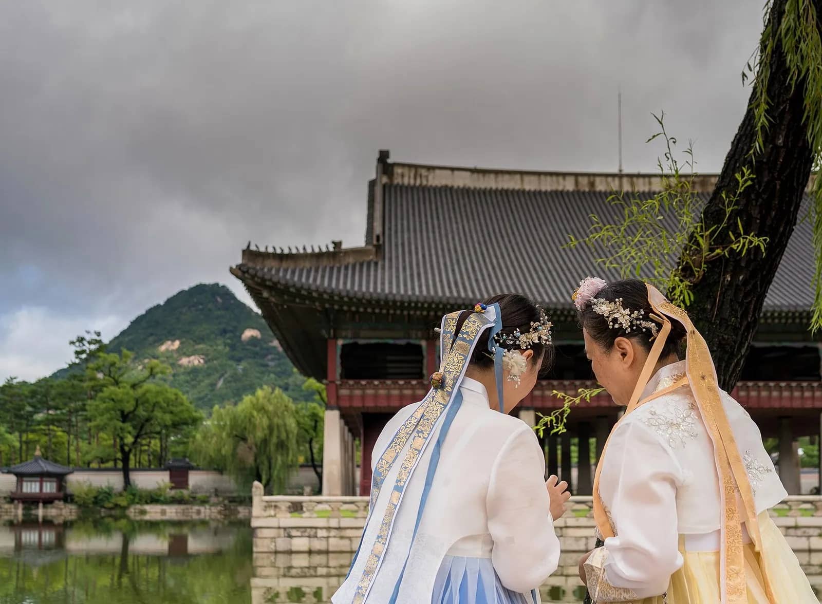 Two visitors in hanbok seen from behind beside Gyeonghoeru pavilion at Gyeongbokgung Palace