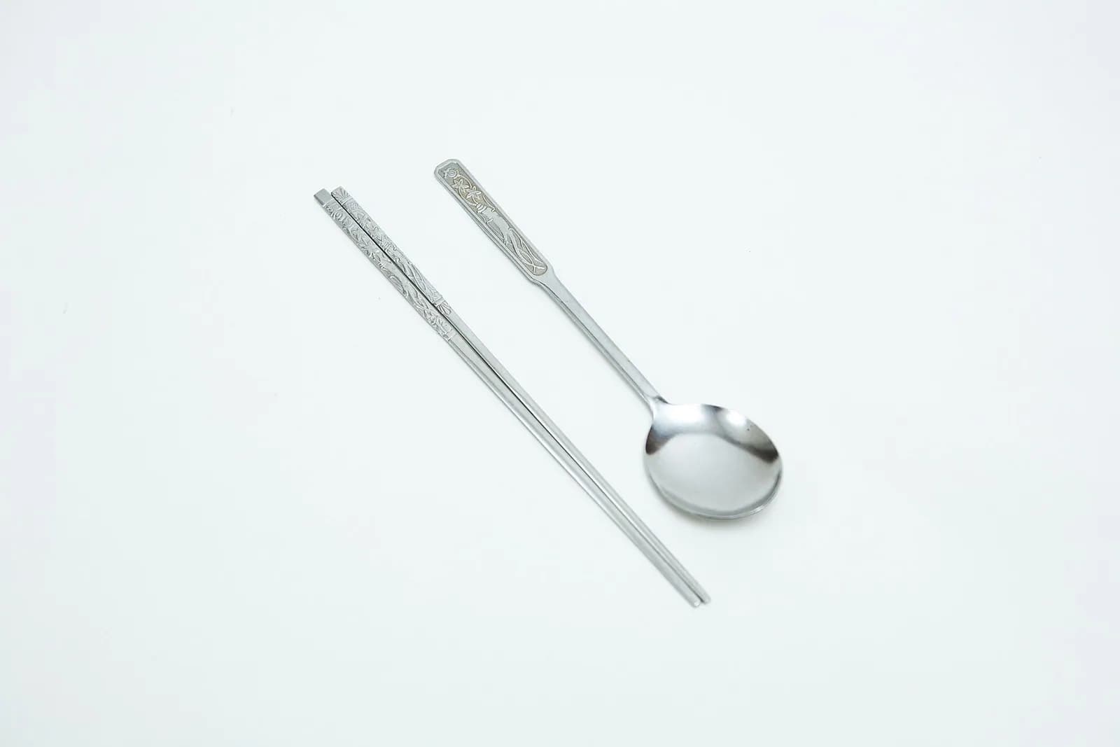 Korean sujeo set of a metal spoon and flat metal chopsticks on a white surface