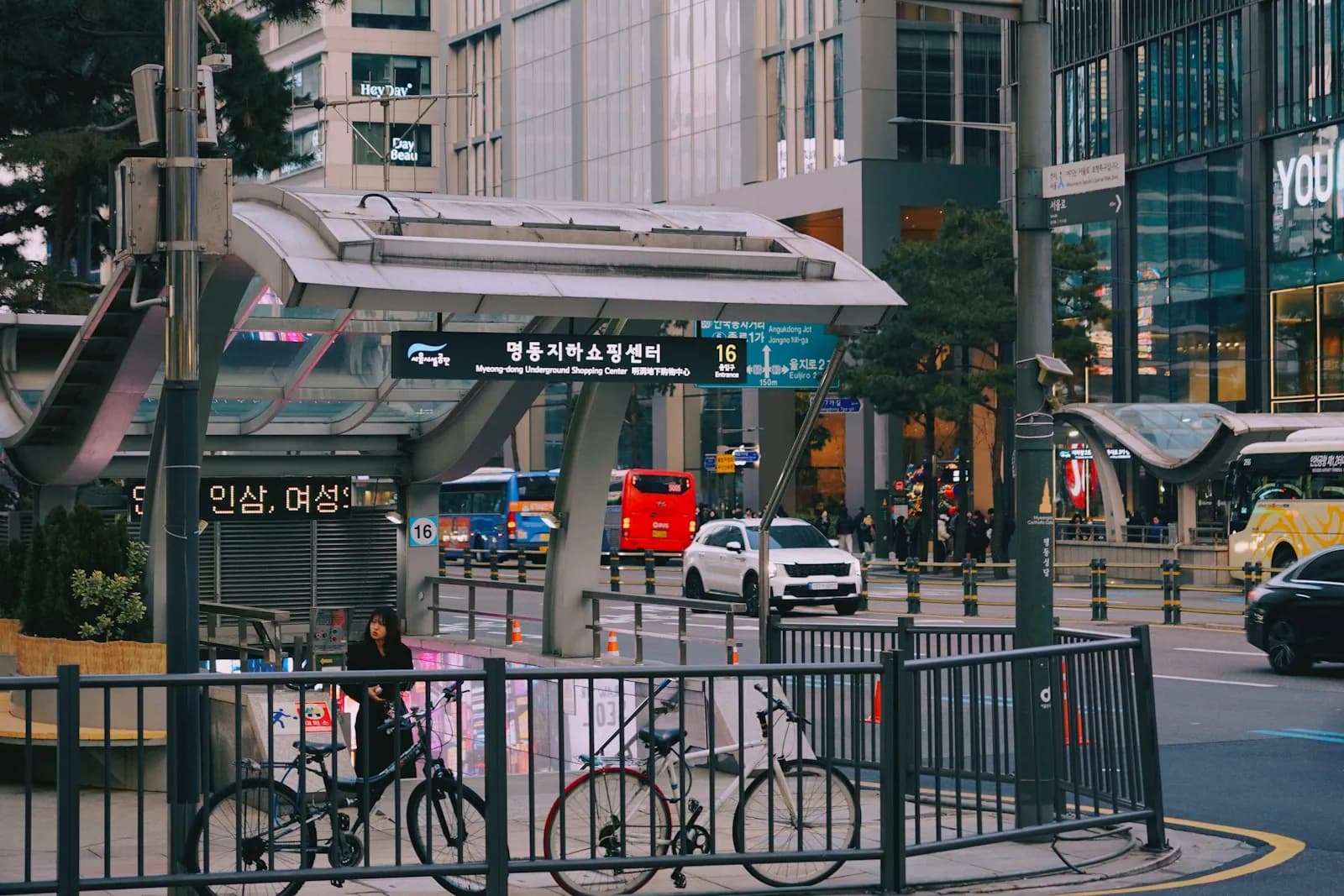 Street-level exit of Myeong-dong Station beside evening traffic and tall buildings