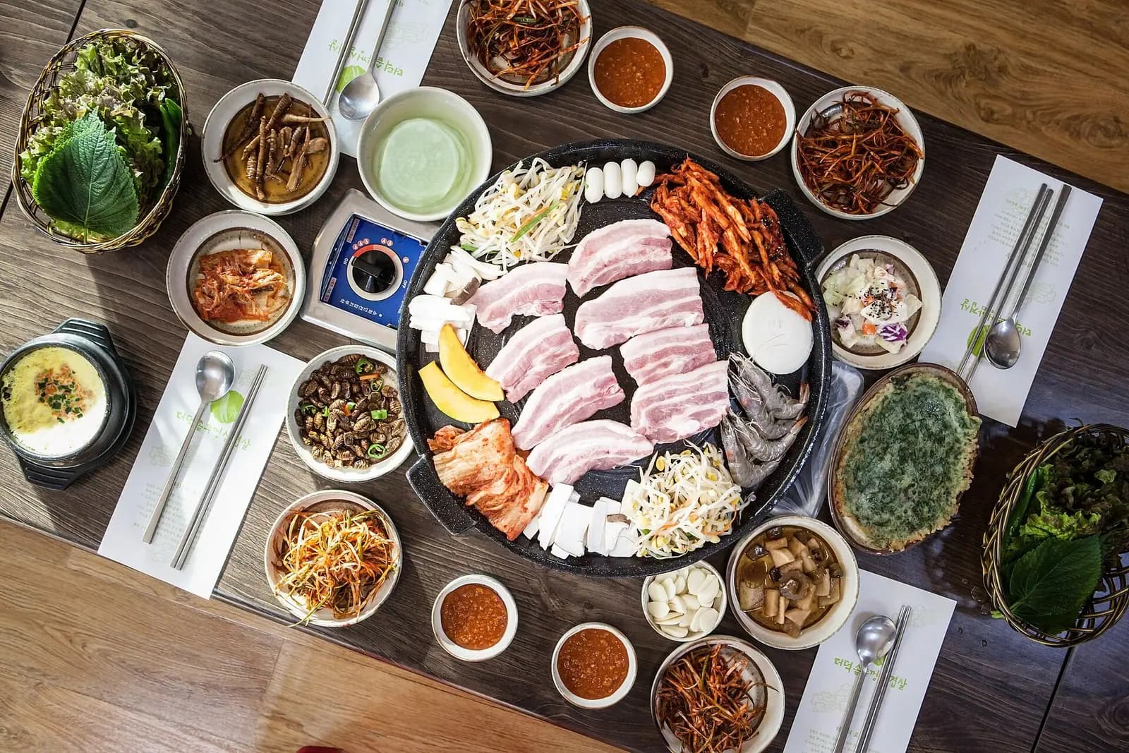 Korean barbecue table seen from above with pork belly on a round grill surrounded by side dishes