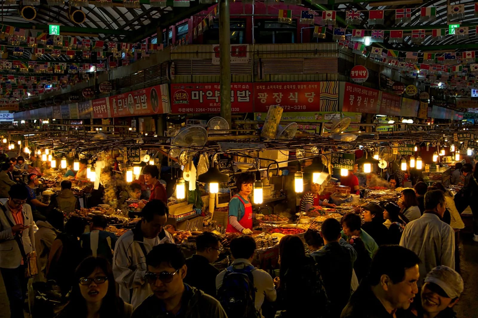 夜晚首爾有頂棚的市場裡擁擠的美食巷,上方是成排的暖色燈光